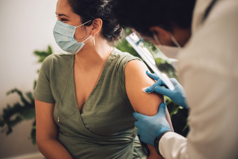 Woman with face mask looking away while doctor giving vaccination.