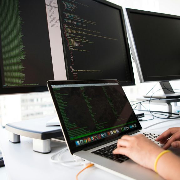 A person typing on a laptop connected with three monitors.