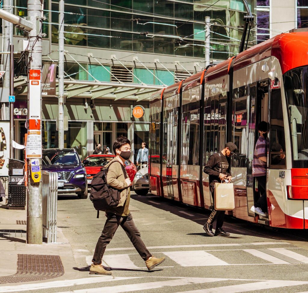 A person wearing a face mask crossing the street in front of a streetcar.