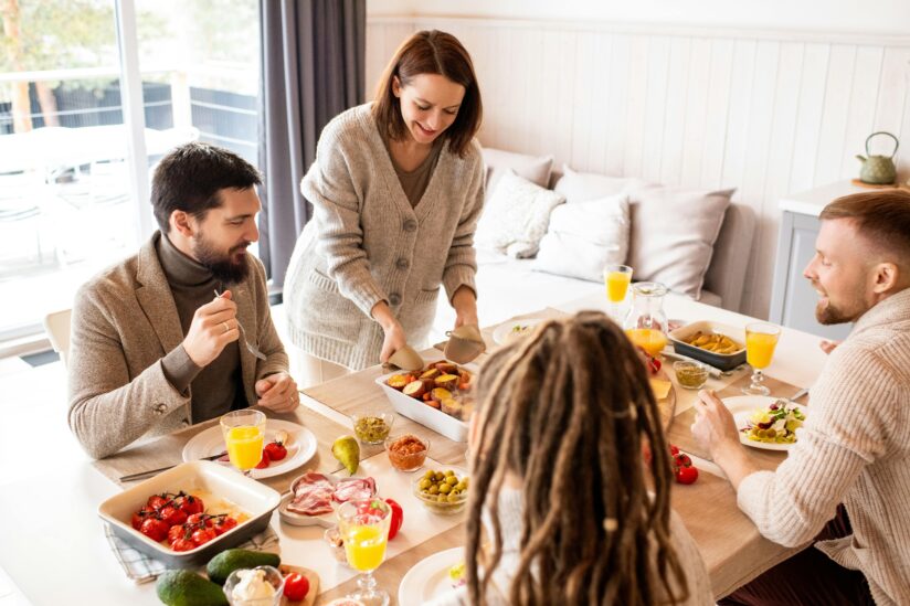 Photo of woman holding a casserole dish and serving to a table of other smiling people.